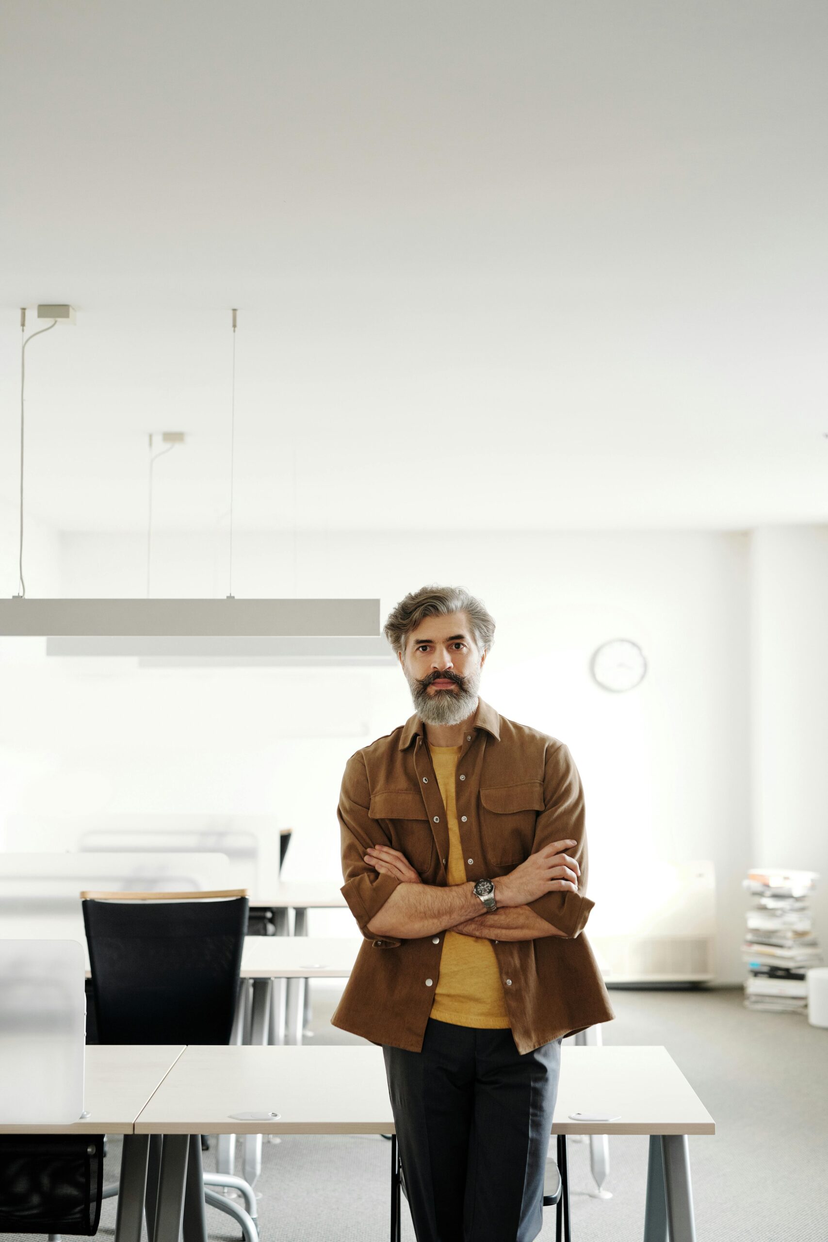 Businessman with crossed arms stands confidently in modern office space, showcasing leadership.